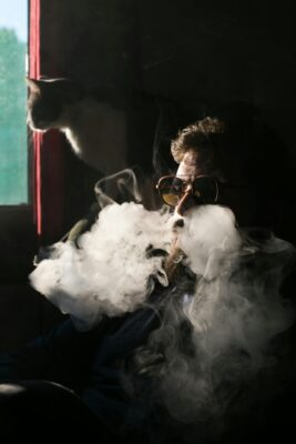 A man smoking a cigarette, surrounded by various Backpackboyz cannabis products and flavors.