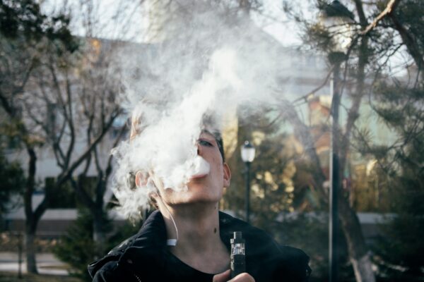 A woman is exhaling vapor from an electronic cigarette, showcasing a modern smoking alternative in a casual setting.